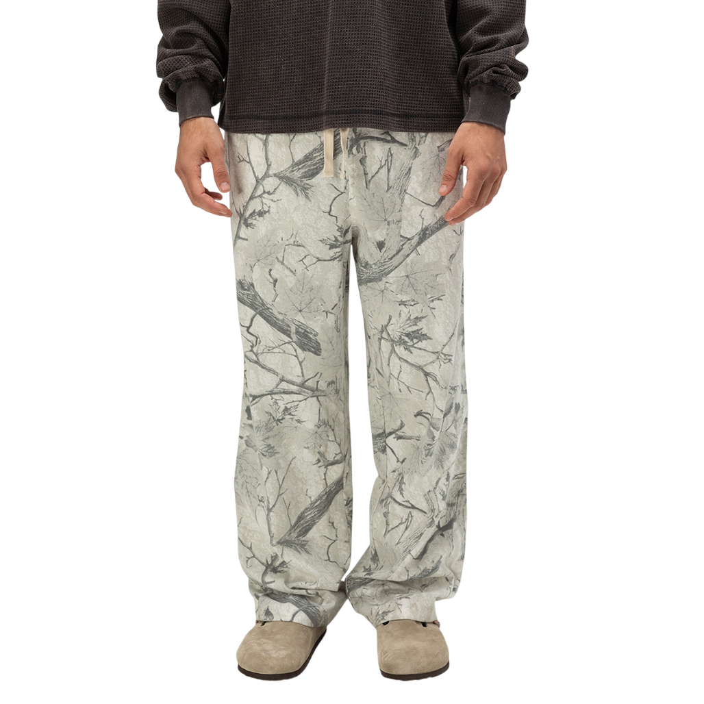 Gray sweatpants featuring a nature-inspired branch and leaf pattern, paired with light brown suede shoes and a dark long-sleeve top.