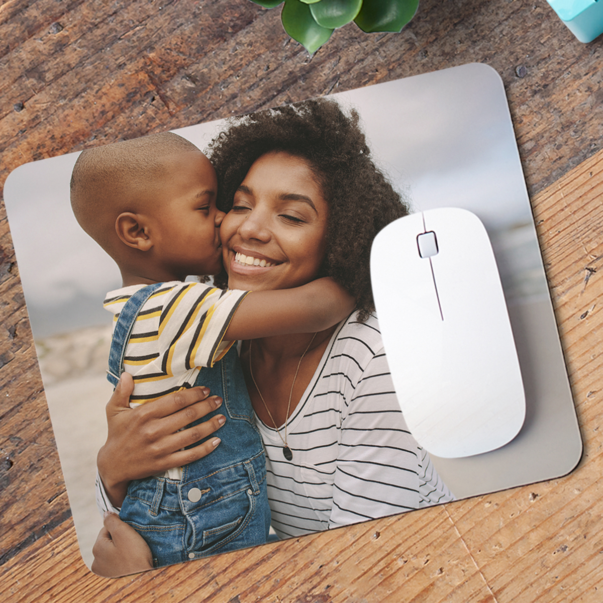 A mouse pad featuring a heartwarming custom photo of a mother and child sharing a joyful moment, accompanied by a modern white mouse on a wooden surface.