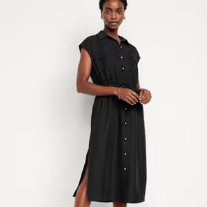 A woman is wearing a waist-defined, sleeveless black shirt dress with a button-down front and a collar, featuring a tie belt at the waist.