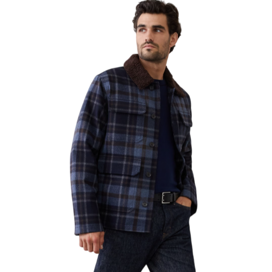 A man is wearing a blue and brown plaid jacket with a shearling collar, dark jeans, and black leather boots.