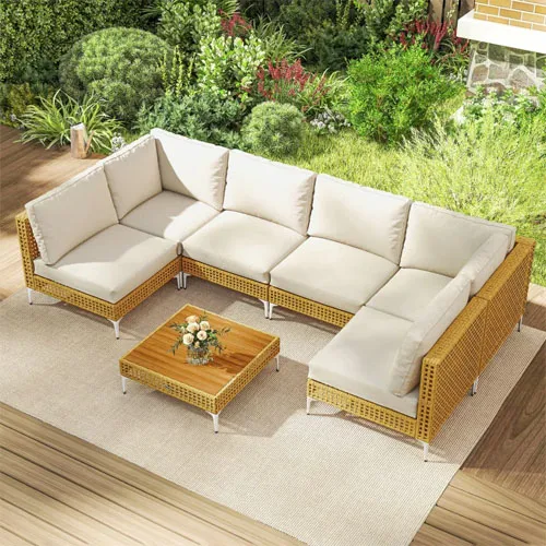 Outdoor wicker sectional sofa with beige cushions and a matching wooden coffee table on a deck surrounded by greenery.