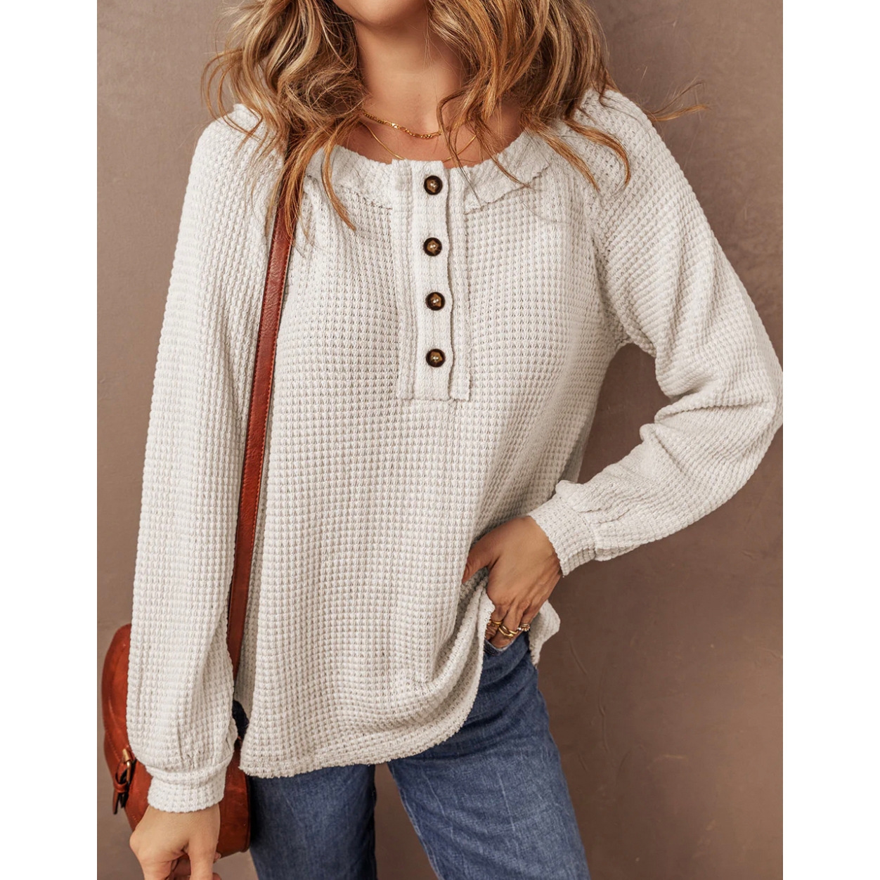 A long-sleeve waffle-knit top featuring a round neckline with a button detail and a loose fit.