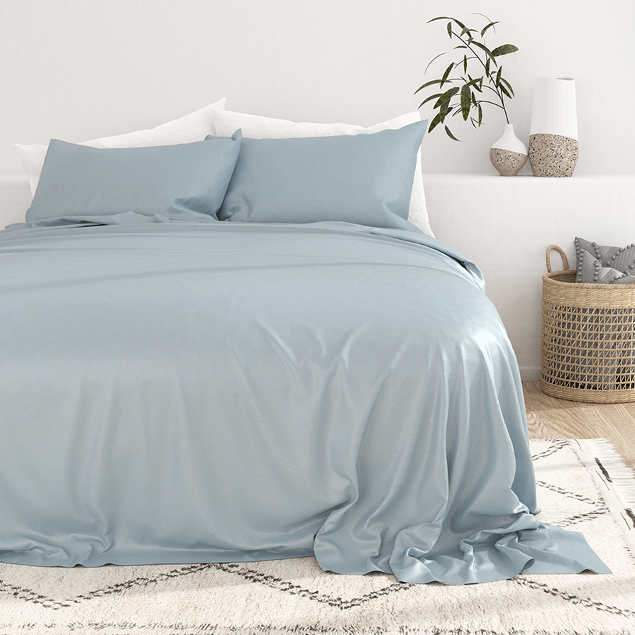 Cooling bamboo sheet sets in a soft blue color, featuring smooth and draped fabric with two matching pillowcases on a neatly made bed. The setting includes decorative vases, a small plant, and a woven basket, creating a minimalist and cozy atmosphere.