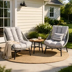 Outdoor patio setup with two cushioned lounge chairs and a small round table on a round woven rug, placed on a concrete surface beside a house with sliding glass doors and surrounded by greenery.