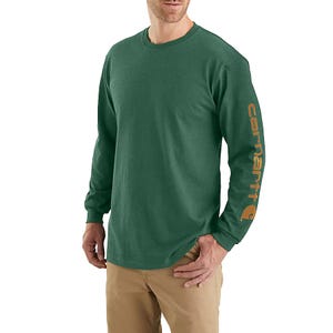 Green long-sleeve Carhartt tee with the brand's logo in brown text down the left sleeve, features a crew neck and relaxed fit. Paired with tan pants.