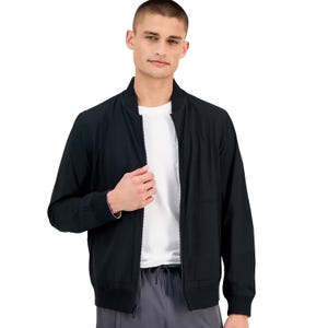 A man is wearing a black zip-up bomber jacket over a white T-shirt, paired with gray drawstring pants.