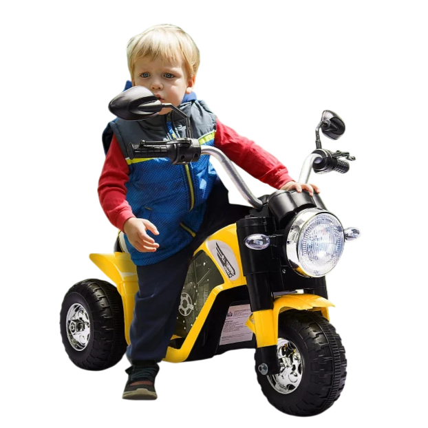 A child is riding a small, yellow, three-wheeled electric motorcycle with a headlight and rear-view mirrors, outdoors on a paved path surrounded by greenery.