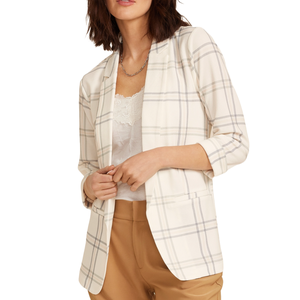 A woman is wearing a cream plaid blazer over a white lace-trimmed top, paired with tan trousers.