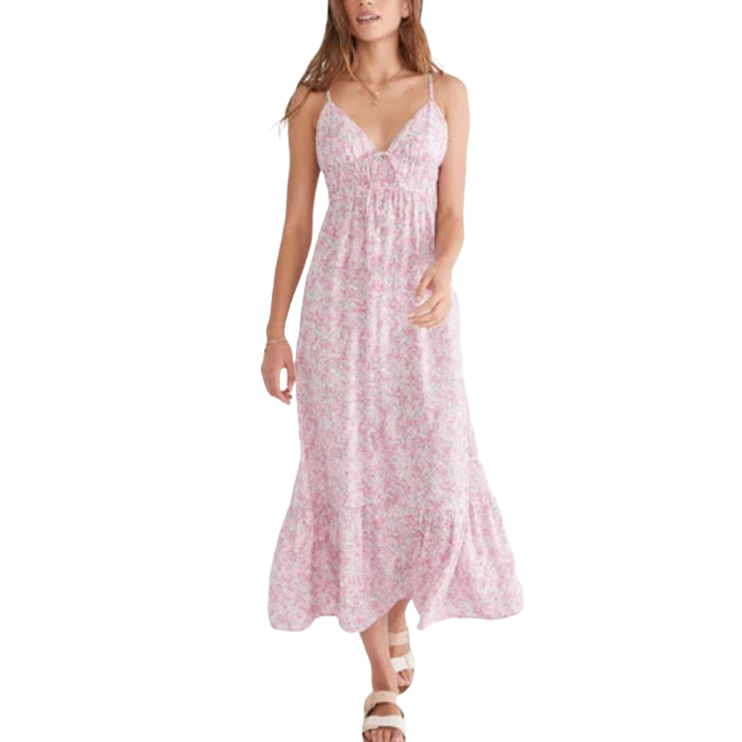 A pink floral V-neck maxi dress with spaghetti straps and an empire waistline, featuring a flowy, ankle-length skirt. The model is also wearing tan sandals.