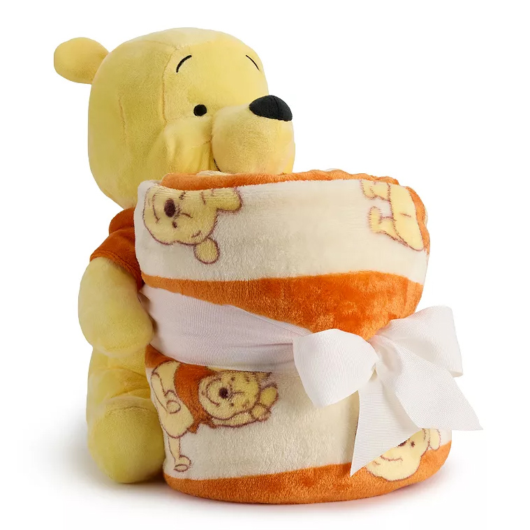 A plush character holds a soft, orange and cream fleece throw blanket, featuring the same character design, wrapped with a white ribbon.