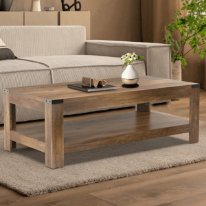 Wooden coffee table with metal accents, featuring a lower shelf and topped with a vase and magazines, placed on a beige carpet in front of a sectional sofa.