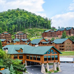 A large, rustic resort complex nestled in a wooded hillside, featuring multiple multi-story log-style buildings with green roofs.
