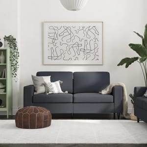A modern living room setting with a dark blue sofa, a green bookshelf, and a brown leather pouf on a white rug.