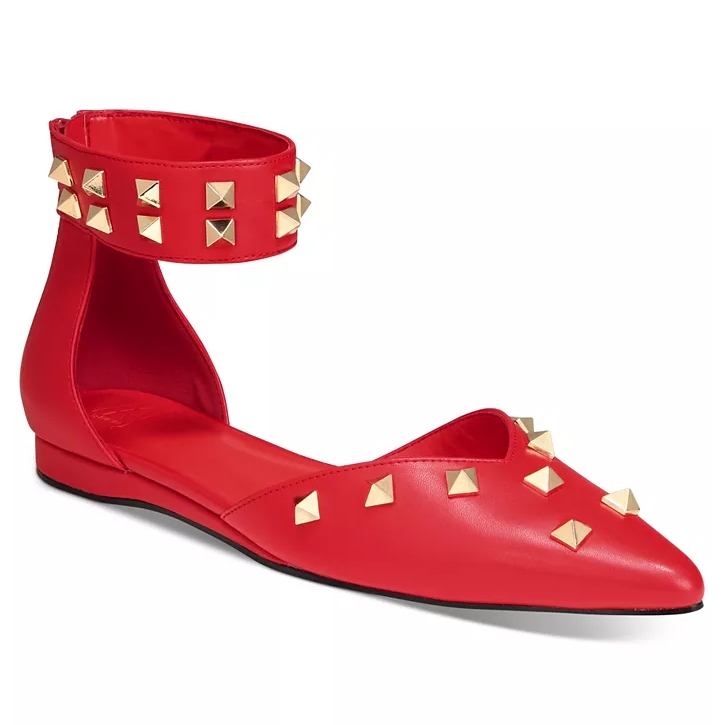 Red flat shoe with a pointed toe, featuring gold stud embellishments and an ankle strap adorned with similar studs.