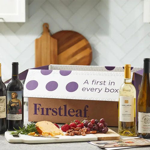 A Firstleaf subscription box is displayed on a kitchen counter alongside a selection of wines, cheese, and fruit.