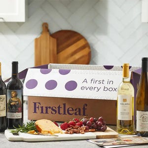 A Firstleaf subscription box is displayed on a kitchen counter alongside a selection of wines, cheese, and fruit.
