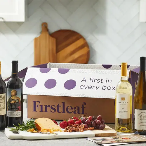 A Firstleaf subscription box is displayed on a kitchen counter alongside a selection of wines, cheese, and fruit.