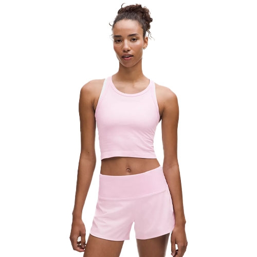 A woman is wearing a light pink workout outfit consisting of a sleeveless crop top with a racerback design and matching high-waisted shorts.