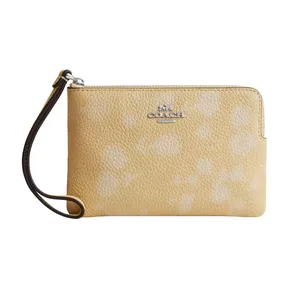 Yellow Coach wristlet with pebbled leather texture, featuring a subtle floral print and a metal logo.