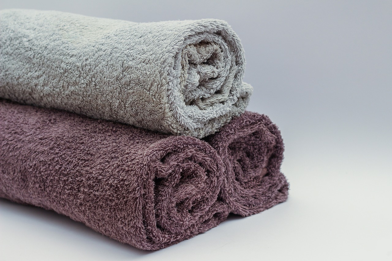 Three rolled towels in gray and shades of purple on a light background.