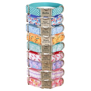 A stack of colorful pet collars with metal buckles engraved with pet names and contact numbers, featuring various patterns such as checkered, floral, and abstract designs.