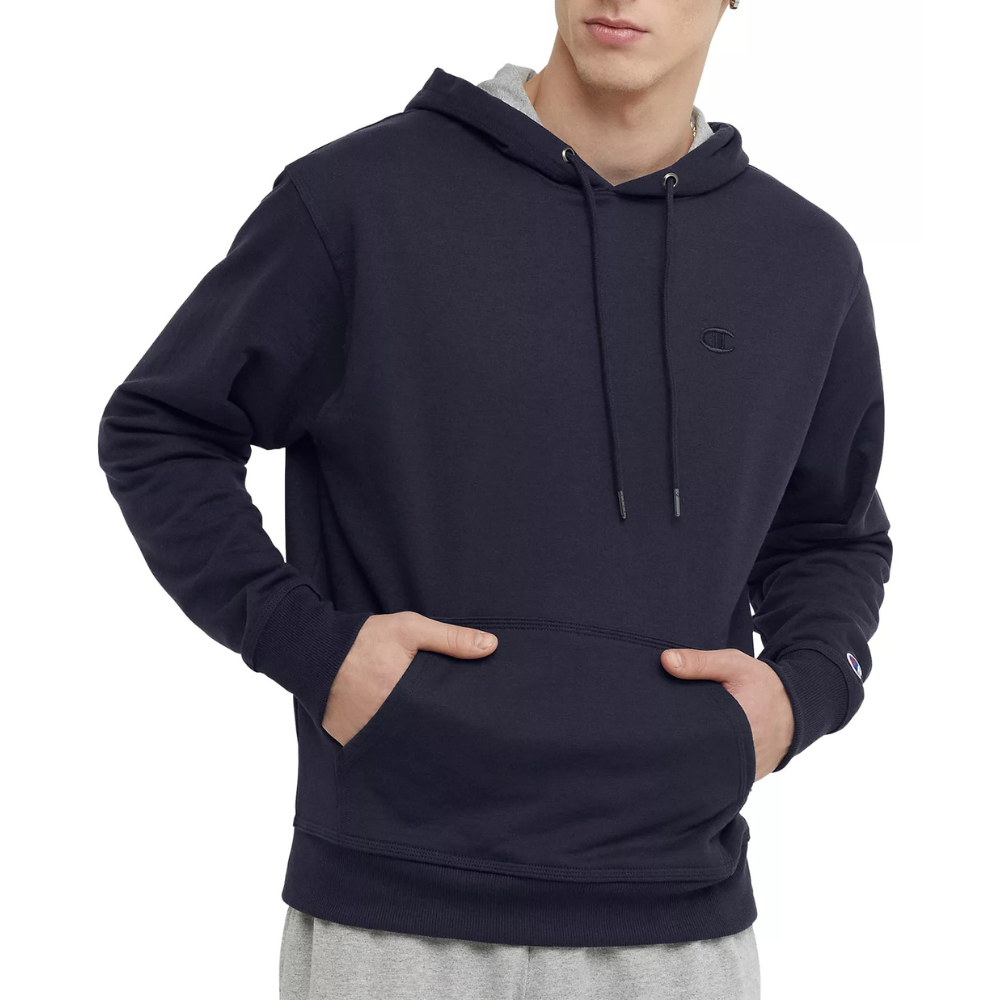 A person is wearing a dark navy hoodie with a small embroidered logo and drawstrings, paired with light gray sweatpants.