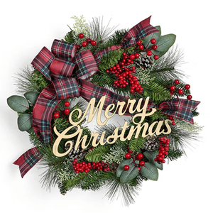 A Christmas wreath features red berries, green foliage, plaid ribbons, and pinecones with a wooden \“Merry Christmas\“ sign in the center.