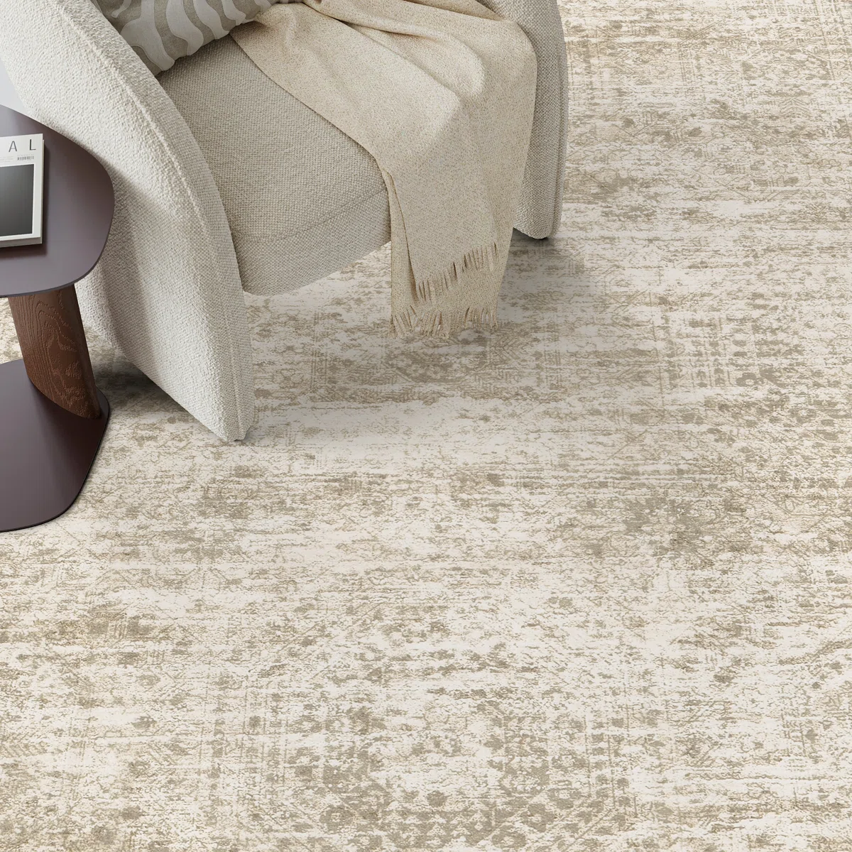 A beige patterned area rug is paired with a light-colored textured armchair and a dark wood side table, topped with a book and light beige throw.