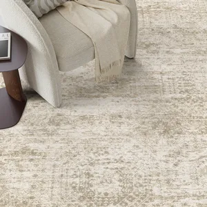 A beige patterned area rug is paired with a light-colored textured armchair and a dark wood side table, topped with a book and light beige throw.