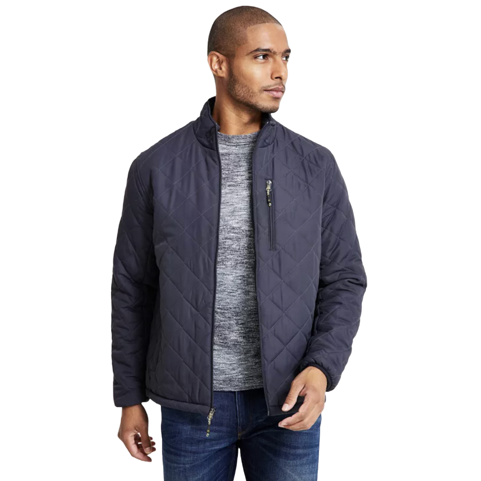 A man is wearing a quilted jacket in a dark color with a zippered chest pocket, over a gray sweater and jeans.