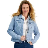A woman is wearing a light blue denim jacket over a white shirt, paired with dark blue jeans.