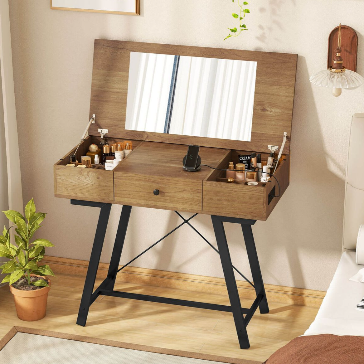 A wooden vanity table with a flip-up mirror, featuring black metal legs, is organized with various cosmetics, a phone stand, and a small potted plant nearby.