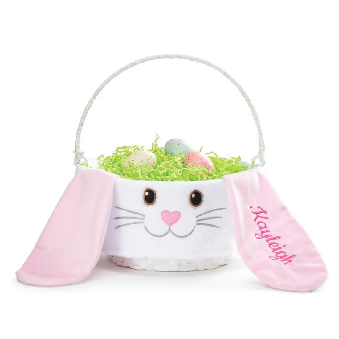 A white basket designed like a bunny face with pink ears, one ear embroidered with \“Kayleigh.\“ It contains green shredded paper and three speckled eggs.