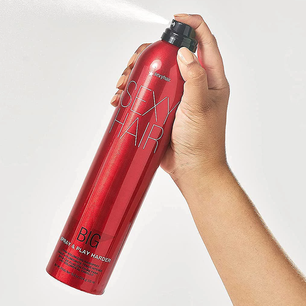 A hand is holding a red can of Sexy Hair Big Spray & Play Harder hairspray.