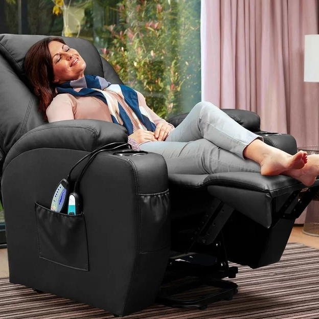 A woman is relaxing in a black leather recliner with an extended footrest, next to a window with curtains.