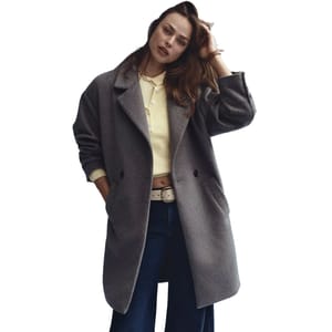 A grey, relaxed-fit, double-breasted coat with a wide collar, large pockets, and slouchy sleeves is worn over a yellow cropped top, dark jeans, and a white belt.