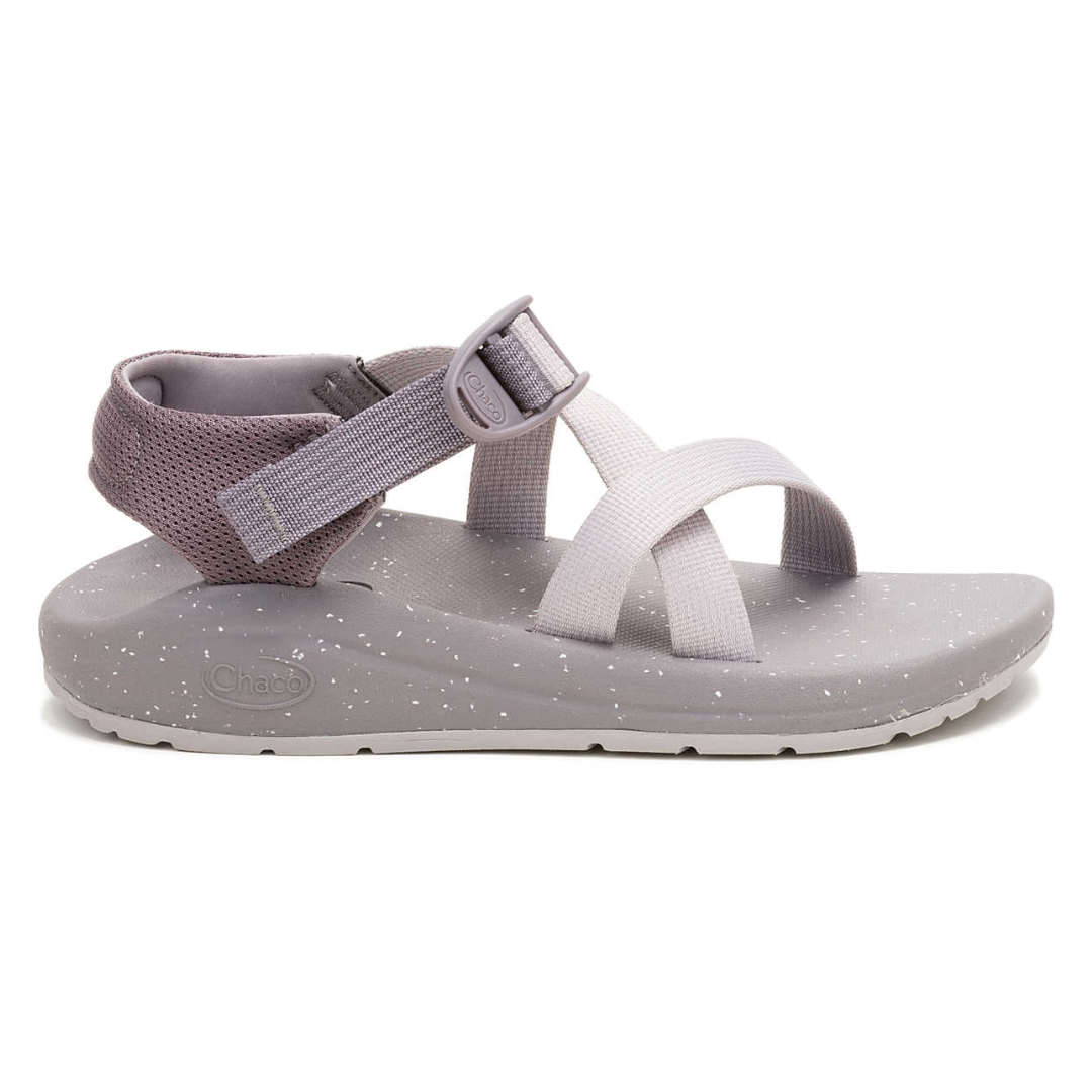 A gray sandal with criss-cross straps, adjustable ankle strap, and speckled sole. Logo visible on the side.
