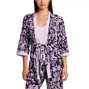 A woman is wearing a three-piece sleep set comprising a floral patterned robe with a tie waist, matching pants, and a plain light purple tank top.