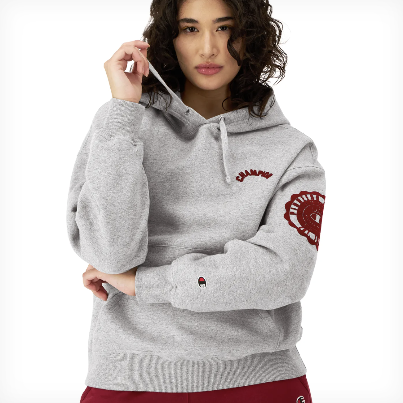 A person wearing a gray Champion hoodie with red logo details on the left chest and sleeve.