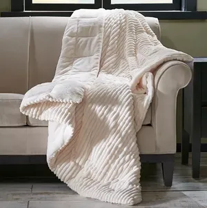 Madison Park Oversized Corduroy Throw is a plush, cream-colored blanket featuring a textured, corduroy pattern, draped over a beige sofa. It's designed for comfort and warmth with a luxurious feel.