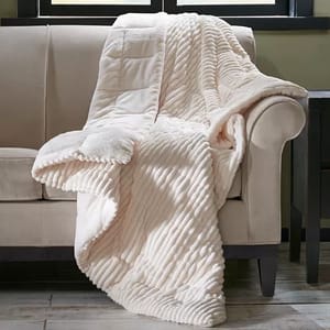 Madison Park Oversized Corduroy Throw is a plush, cream-colored blanket featuring a textured, corduroy pattern, draped over a beige sofa. It's designed for comfort and warmth with a luxurious feel.