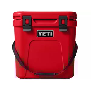 Red YETI cooler with a black carry strap and secure latch closures, designed for durable outdoor use.