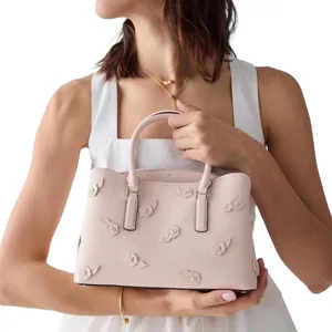 A person is holding a pink handbag with floral 3D embellishments. The handbag has a structured design, dual handles, and subtle branding.