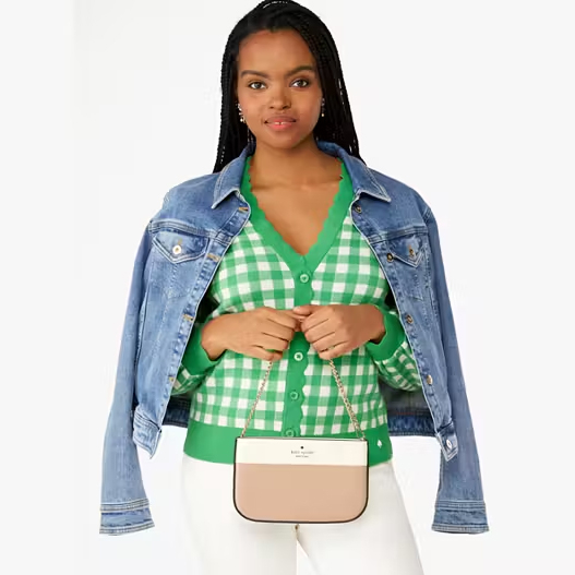 A woman is wearing a green checked shirt, a blue denim jacket, and holding a two-tone shoulder bag.