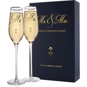 Two champagne flutes labeled \“Mr\“ and \“Mrs\“ are in front of a box that says \“Mr. & Mrs. Premium Champagne Glasses\“ and includes the phrase \“to love, to happiness, to good life.\“