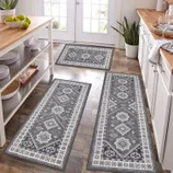 Three gray patterned kitchen rugs are placed on a wooden floor, featuring geometric and floral motifs, positioned in front of cabinets and a kitchen island.