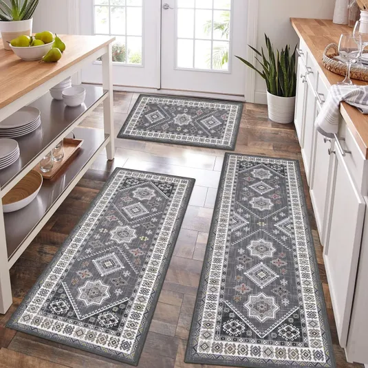 Three gray patterned kitchen rugs are placed on a wooden floor, featuring geometric and floral motifs, positioned in front of cabinets and a kitchen island.
