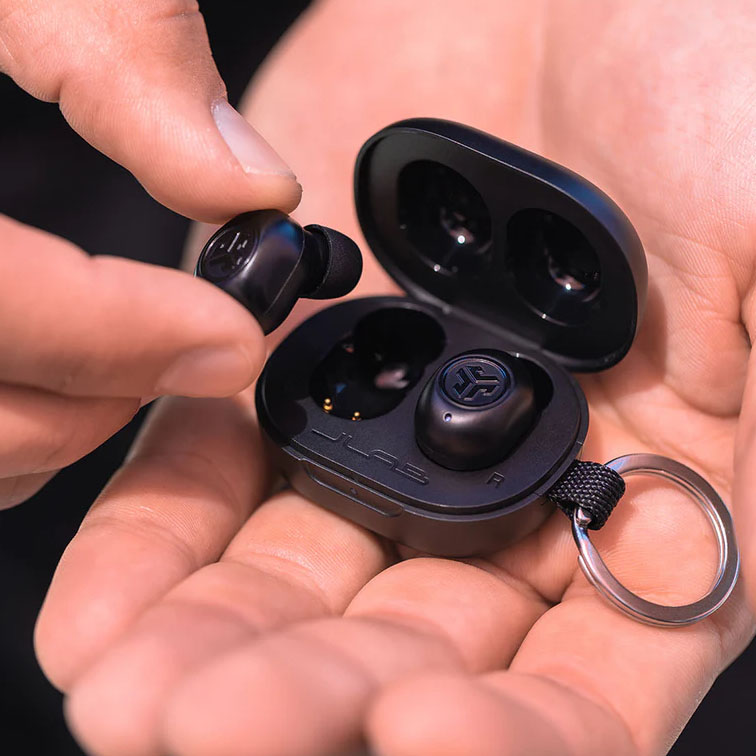 A pair of black JLab Mini wireless earbuds are shown being taken out from their compact charging case, which is held in a person's hand.