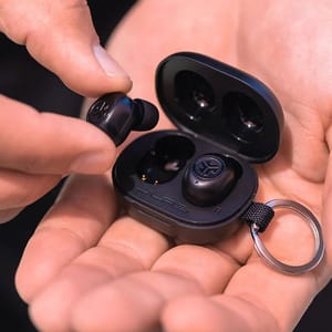 A pair of black JLab Mini wireless earbuds are shown being taken out from their compact charging case, which is held in a person's hand.