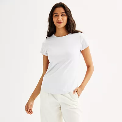 A woman is wearing a plain white crewneck tee with short sleeves, paired with light-colored pants.